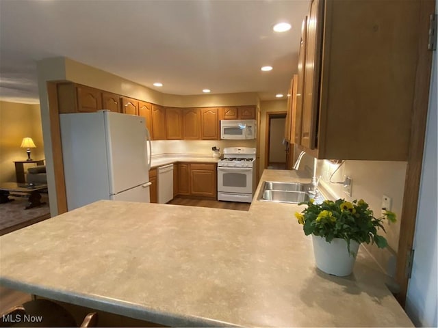 kitchen with a sink, light countertops, white appliances, and a peninsula