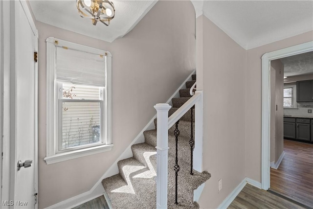 staircase featuring baseboards, a notable chandelier, and wood finished floors