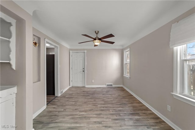 empty room featuring visible vents, baseboards, a ceiling fan, and wood finished floors