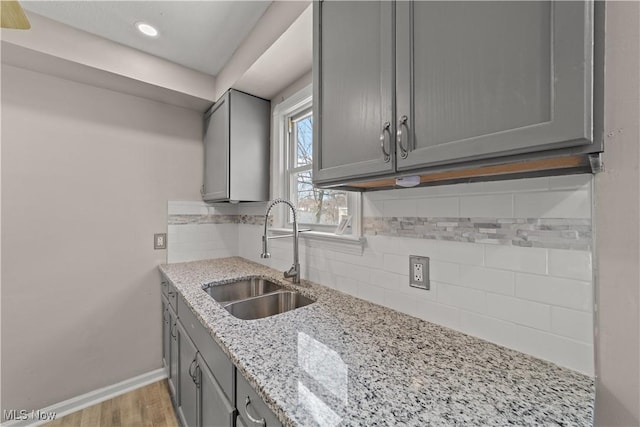 kitchen with tasteful backsplash, light wood-type flooring, baseboards, gray cabinetry, and a sink