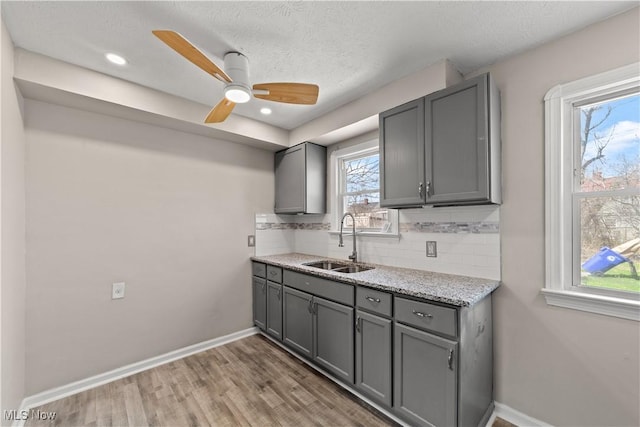 kitchen featuring gray cabinetry, light wood-type flooring, a sink, and backsplash