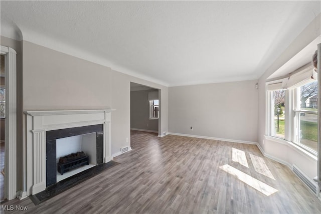 unfurnished living room with a fireplace with flush hearth, visible vents, baseboards, and wood finished floors