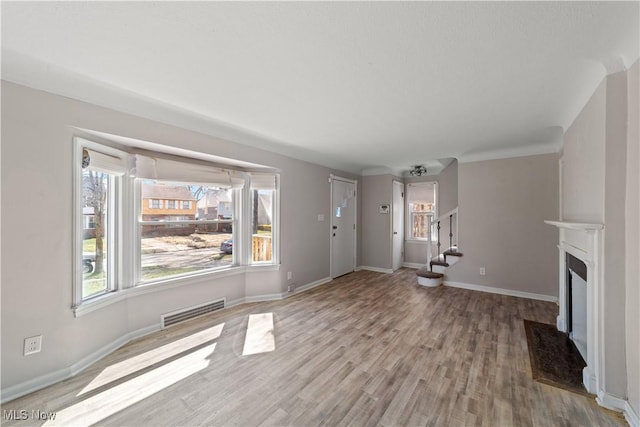 unfurnished living room featuring wood finished floors, baseboards, visible vents, and stairs