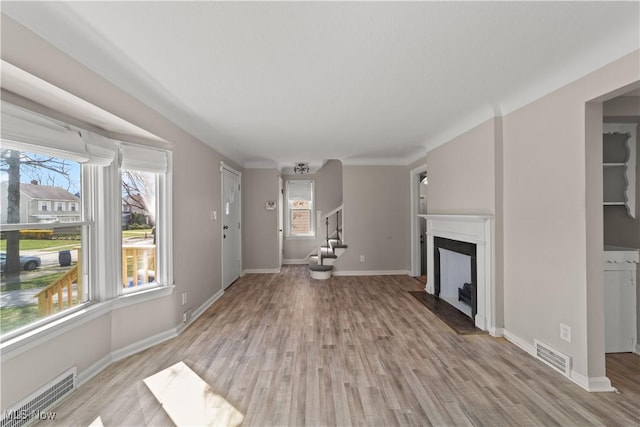 unfurnished living room featuring baseboards, light wood-style floors, a fireplace, and visible vents