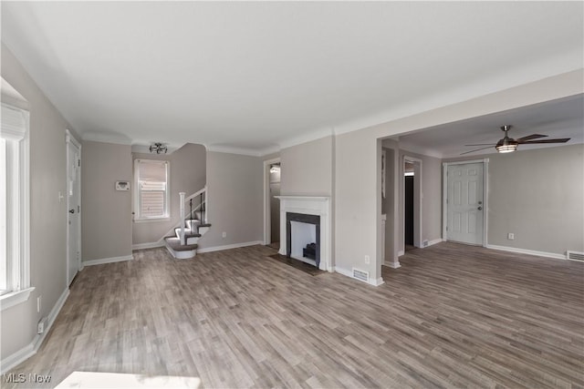 unfurnished living room featuring visible vents, baseboards, a ceiling fan, light wood-style floors, and stairway