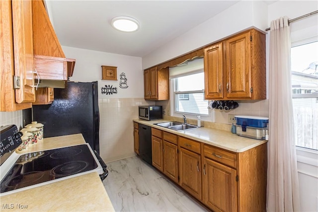 kitchen with black appliances, a sink, light countertops, brown cabinetry, and light marble finish flooring