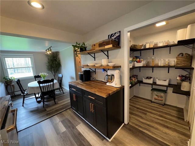 kitchen featuring dark wood-type flooring, butcher block counters, dark cabinetry, and open shelves