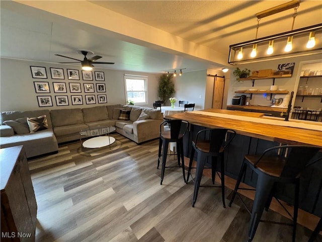 bar with pendant lighting, wood finished floors, ceiling fan, and a barn door