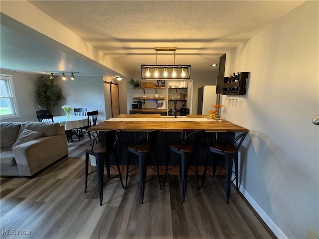 bar featuring a barn door, freestanding refrigerator, a textured ceiling, dark wood-type flooring, and rail lighting