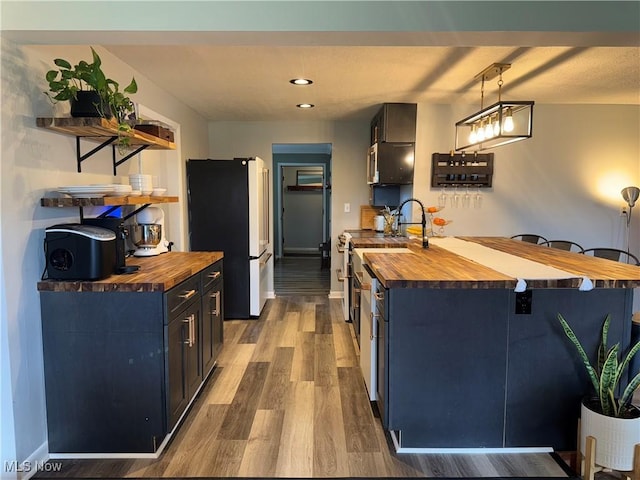kitchen featuring stainless steel range, open shelves, freestanding refrigerator, and butcher block counters