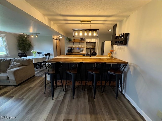bar featuring a textured ceiling, freestanding refrigerator, dark wood finished floors, and a barn door