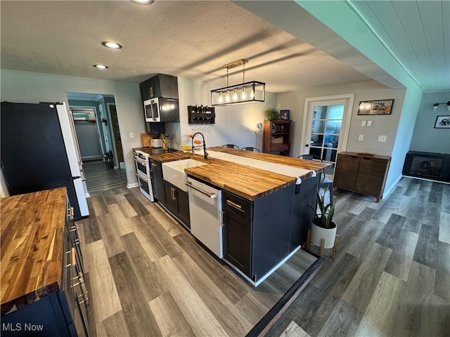kitchen with dark wood-type flooring, a textured ceiling, a sink, stainless steel appliances, and wooden counters