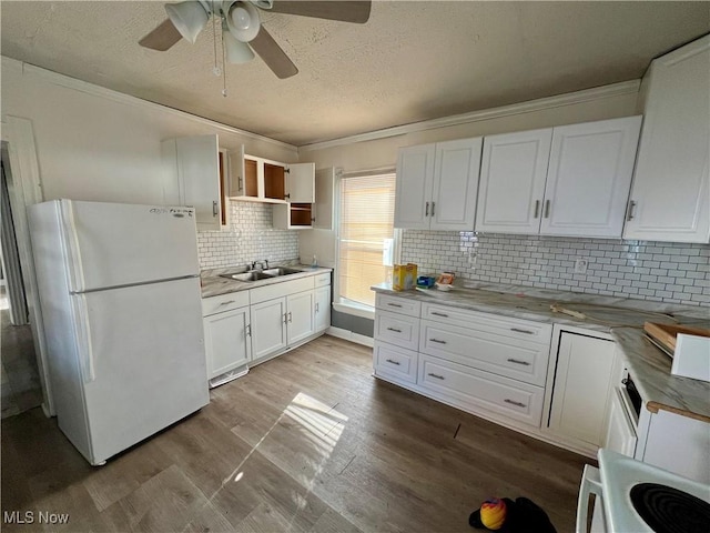 kitchen featuring freestanding refrigerator, a textured ceiling, ornamental molding, white cabinets, and a sink