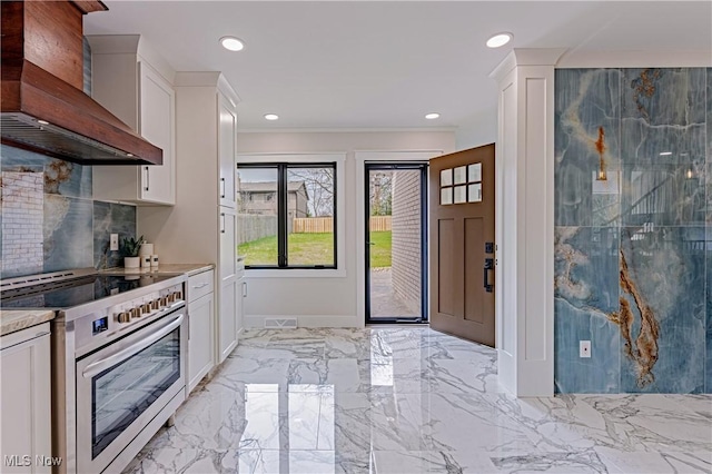 20601 Shelburne Rd, Shaker Heights, OH 44122 - kitchen featuring stainless steel electric range oven, wall chimney range hood, white cabinetry, light countertops, and decorative backsplash