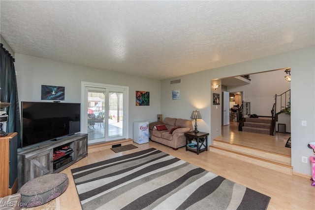 living room featuring stairs, a textured ceiling, visible vents, and wood finished floors