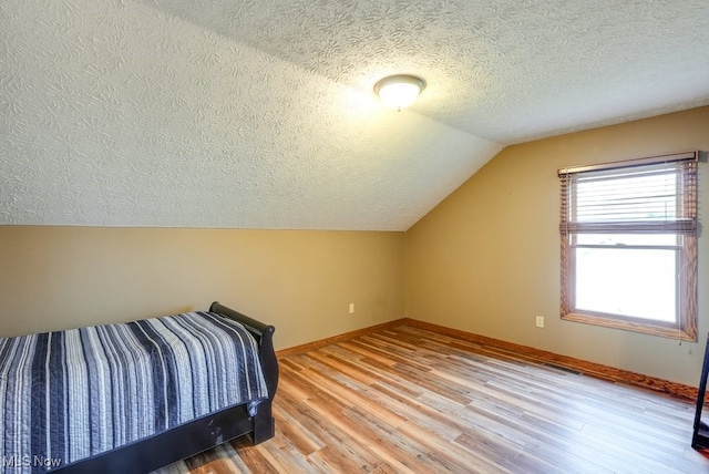 bedroom featuring visible vents, baseboards, a textured ceiling, light wood finished floors, and lofted ceiling