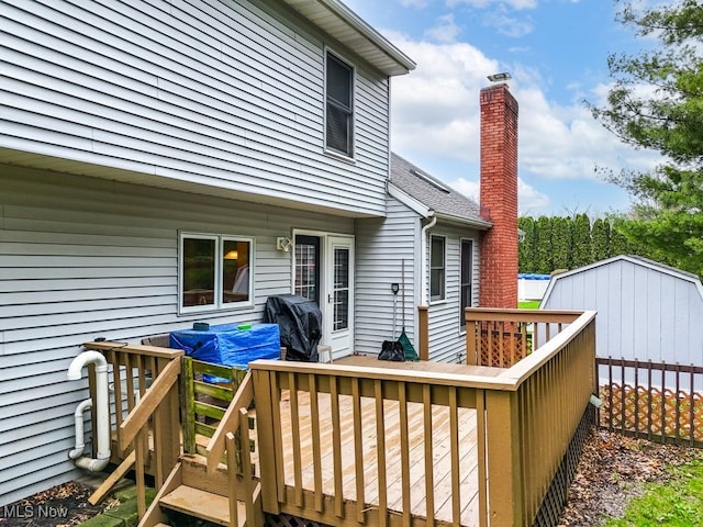 wooden terrace featuring a storage shed, grilling area, and an outbuilding