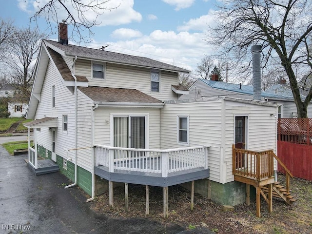 rear view of house featuring a wooden deck, a chimney, and a shingled roof