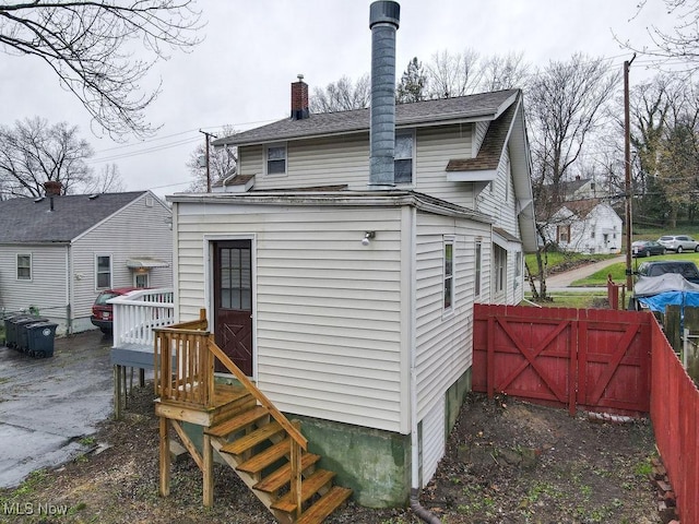 back of house featuring roof with shingles, fence, a gate, and a chimney