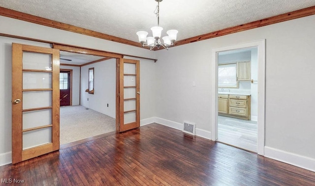 empty room with a chandelier, dark wood-type flooring, visible vents, and a wealth of natural light