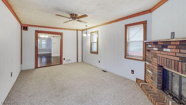 carpeted empty room featuring crown molding, ceiling fan, a textured ceiling, visible vents, and a brick fireplace