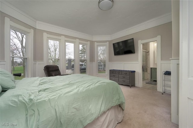 bedroom with a wainscoted wall, ensuite bathroom, light colored carpet, crown molding, and a decorative wall