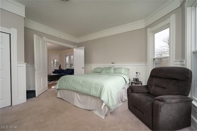 carpeted bedroom featuring a decorative wall, wainscoting, and crown molding