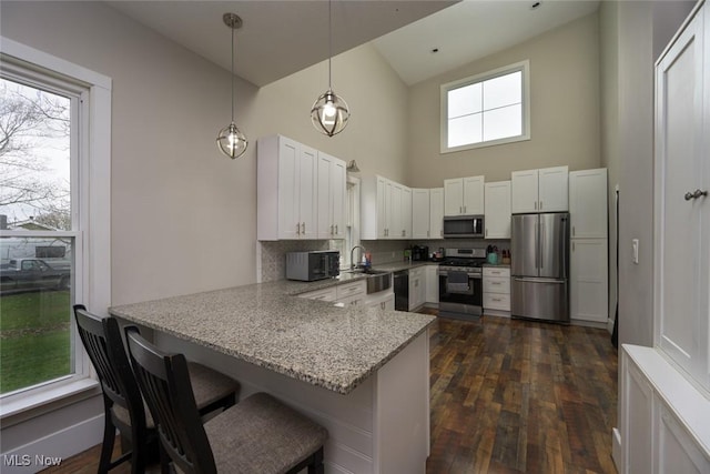 kitchen with white cabinets, a peninsula, stainless steel appliances, high vaulted ceiling, and light stone counters