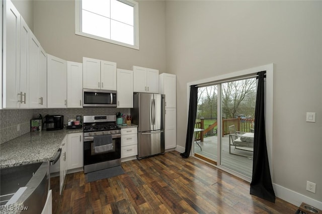 kitchen featuring a towering ceiling, backsplash, white cabinets, and stainless steel appliances
