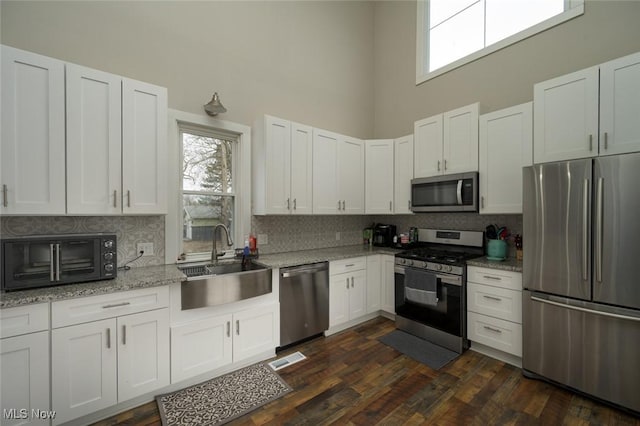 kitchen featuring a sink, white cabinetry, a towering ceiling, stainless steel appliances, and backsplash