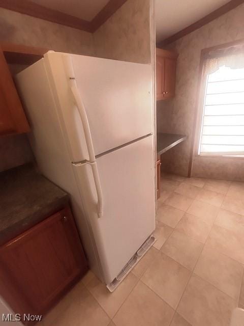 kitchen with light tile patterned flooring, freestanding refrigerator, and ornamental molding