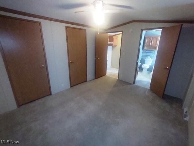 unfurnished bedroom featuring connected bathroom, ornamental molding, light carpet, lofted ceiling, and multiple closets