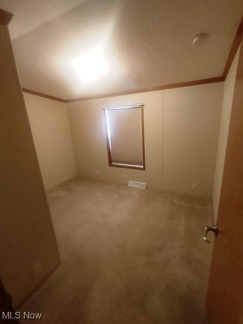 carpeted spare room featuring crown molding, visible vents, and vaulted ceiling