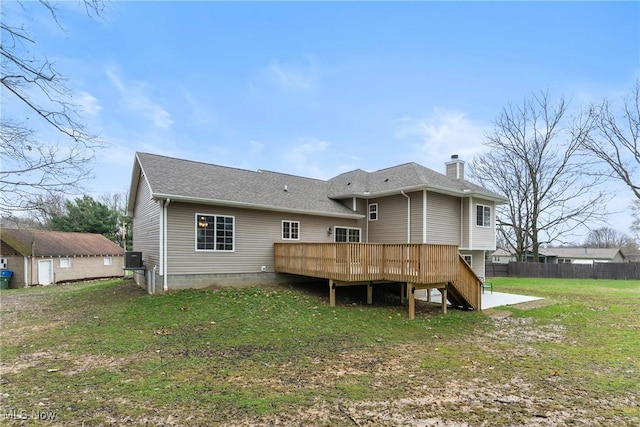 rear view of property featuring a yard, fence, a chimney, a shingled roof, and a deck