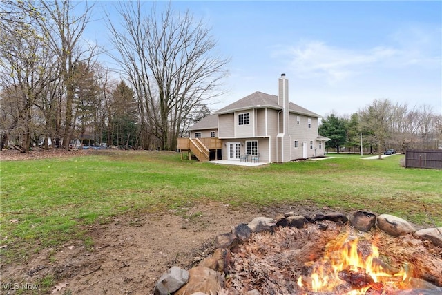 exterior space featuring a patio, a chimney, a fire pit, a deck, and a lawn