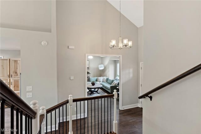 stairs with a chandelier, wood finished floors, high vaulted ceiling, and baseboards