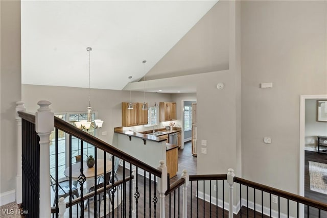 stairway with baseboards, high vaulted ceiling, an inviting chandelier, and wood finished floors