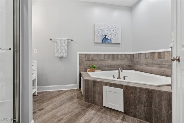 bathroom with a garden tub, wood finished floors, and baseboards