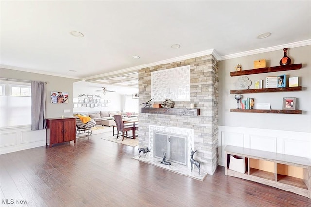 living room featuring a stone fireplace, ornamental molding, wainscoting, ceiling fan, and wood finished floors