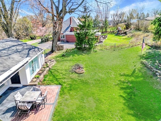 view of yard with a deck, fence, and a fire pit