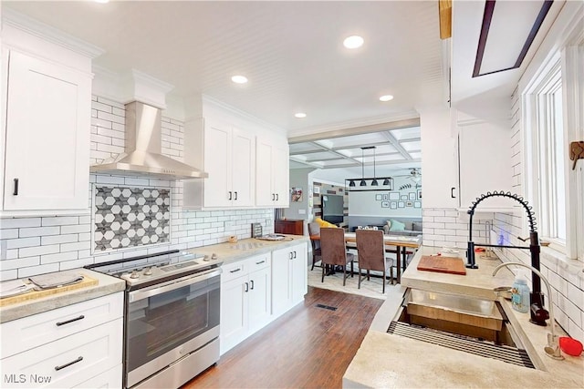 kitchen with stainless steel electric range oven, white cabinets, wall chimney exhaust hood, and a sink