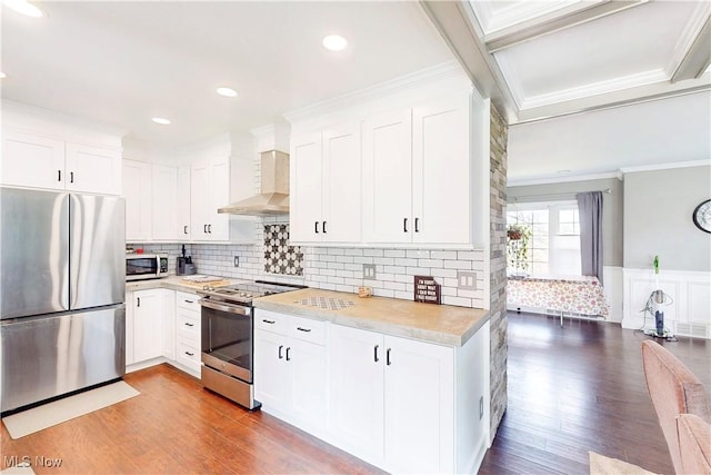 kitchen with crown molding, wall chimney range hood, wood finished floors, and stainless steel appliances