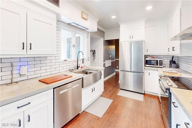 kitchen with light countertops, backsplash, wall chimney exhaust hood, appliances with stainless steel finishes, and a sink