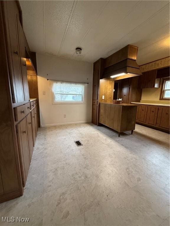 kitchen with a peninsula, a textured ceiling, baseboards, light countertops, and premium range hood