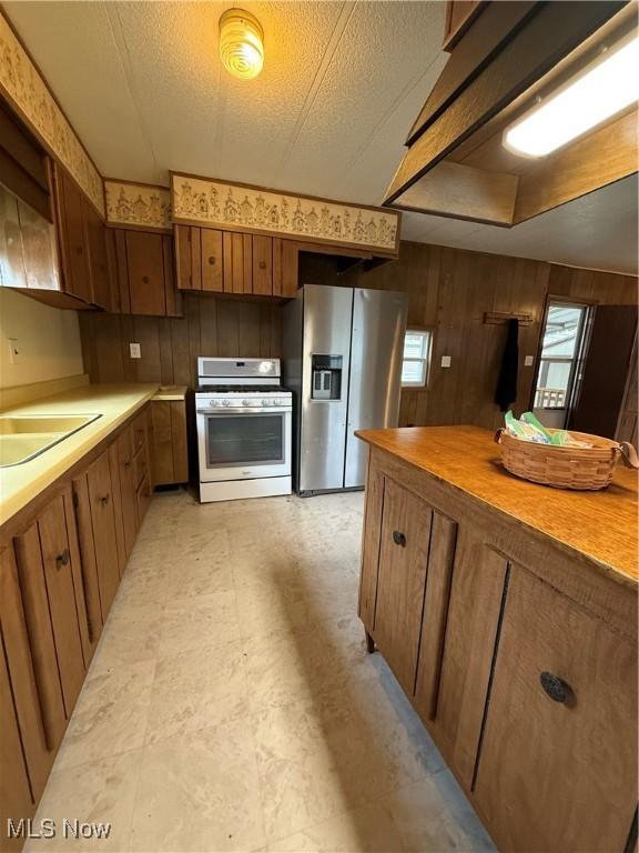 kitchen with stainless steel fridge, gas range gas stove, wood walls, and light floors