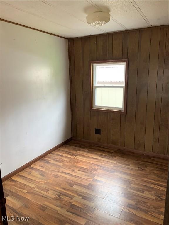 unfurnished room featuring baseboards, wooden walls, and wood finished floors