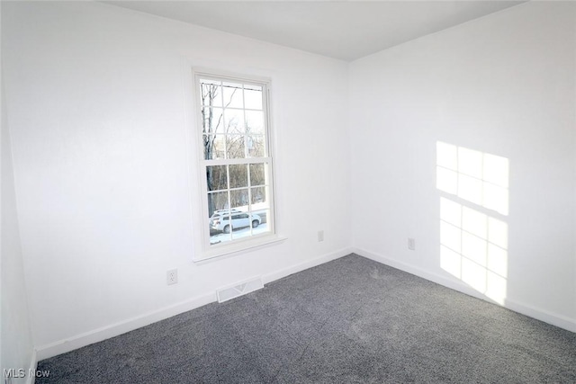 spare room featuring visible vents, baseboards, and dark colored carpet