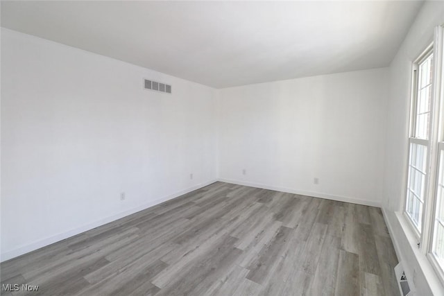 spare room featuring plenty of natural light, visible vents, baseboards, and wood finished floors
