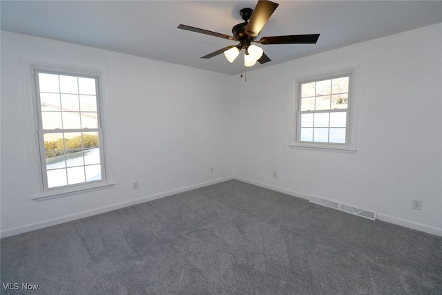 unfurnished room featuring dark carpet, visible vents, baseboards, and plenty of natural light