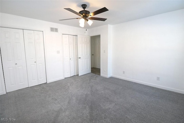 unfurnished bedroom with baseboards, carpet flooring, two closets, visible vents, and ceiling fan
